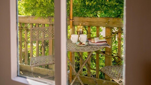 Un terrazzo in legno con un tavolo apparecchiato per due persone, una caffettiera e un giornale.