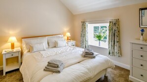 Una camera da letto con un letto, due comodini, una cassettiera, una finestra con tende e vista su del verde all'esterno.