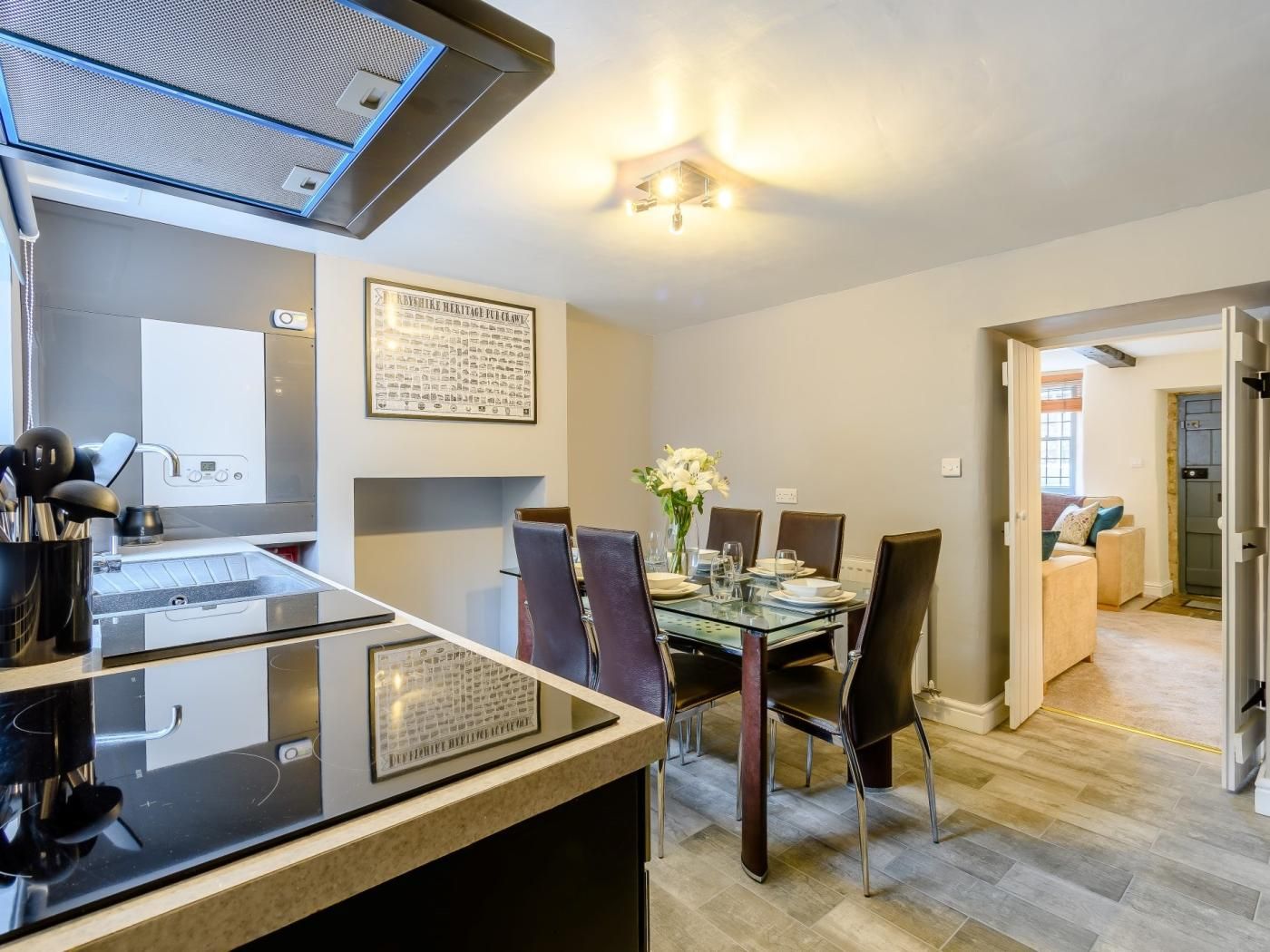 A modern kitchen with a built-in stove, a dining area with a glass table and chairs, and a hallway leading to a living space.