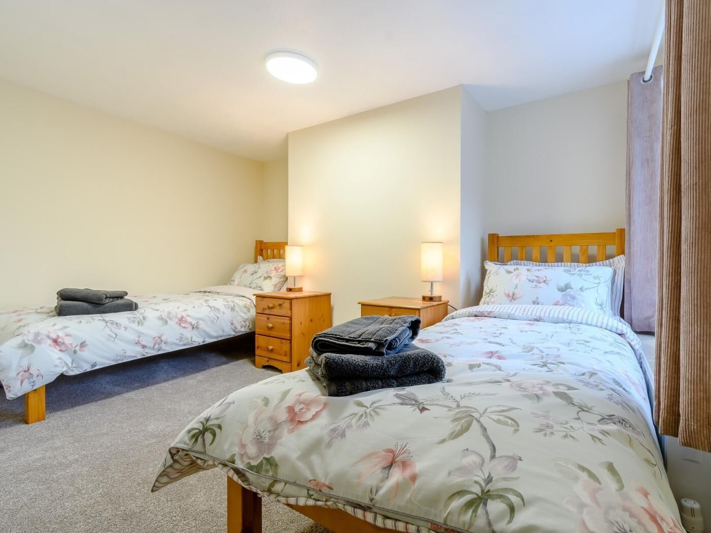 A bedroom with two beds, each with a nightstand and lamp, a wooden headboard, and a carpeted floor.