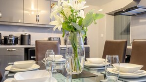 A modern kitchen with stainless steel appliances, a dining table set with white plates and glasses, and a vase with white flowers. - 3 Bed in Matlock (oc-78591) (Cromford)