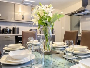 A modern kitchen with stainless steel appliances, a dining table set with white plates and glasses, and a vase with white flowers. - 3 Bed in Matlock (oc-78591) (Cromford)