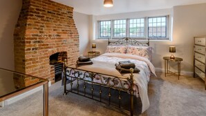 A bedroom with a brick fireplace, a bed with floral bedding, a window with a view, and a dresser. - 3 Bed in Matlock (oc-78591) (Cromford)