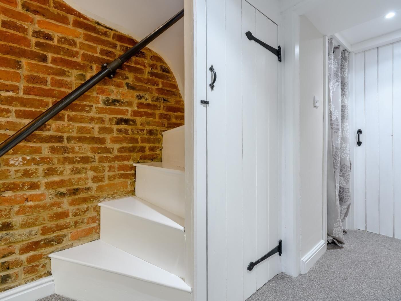 A staircase with white steps and a brick wall, leading to a white door with black handles.