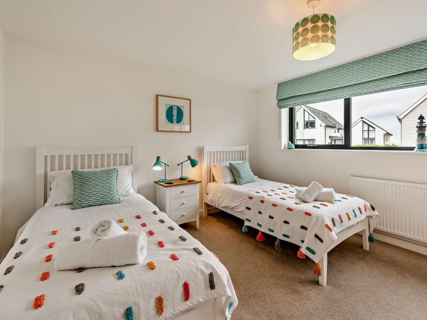 A bedroom with two beds, a window with a view, a lamp, and a framed picture on the wall.
