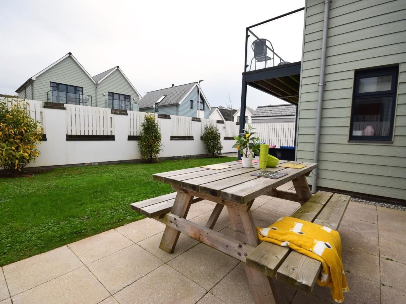 A wooden picnic table with benches, a yellow blanket, and a potted plant.