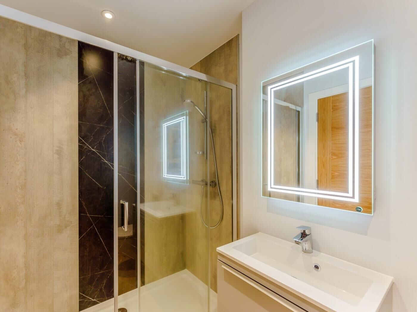 A modern bathroom with a glass-enclosed shower, a white sink, and a mirror with illuminated edges.
