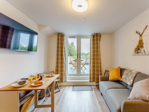 A modern living room with a sofa, a dining table with breakfast items, and a TV mounted on the wall. - 2 Bed in Brockenhurst (oc-78728) (Brockenhurst)