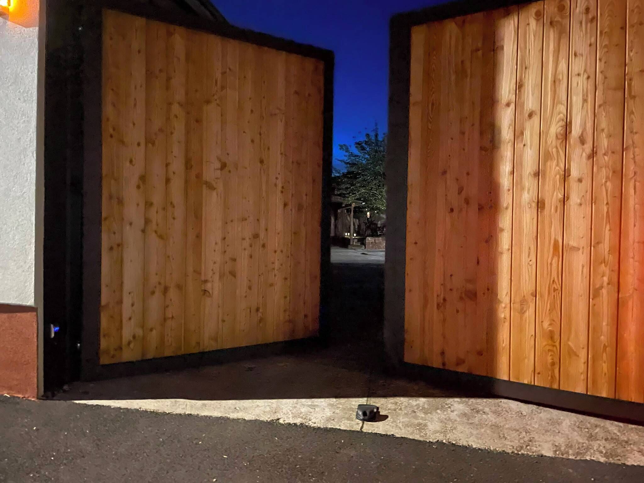 A wooden gate leading to a driveway with a mailbox in the foreground.