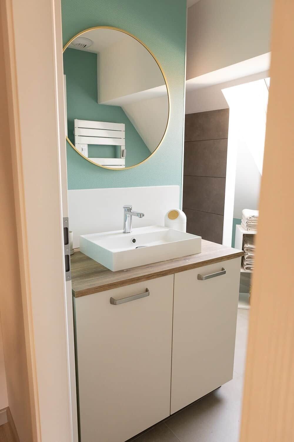 A bathroom with a white sink, a mirror with a gold frame, and a teal accent wall.