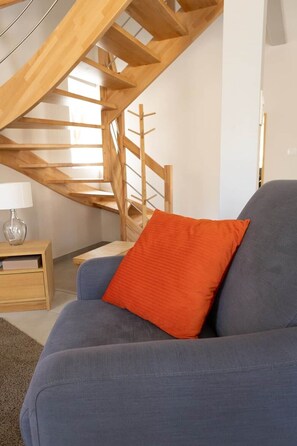 A living room with a blue sofa, a wooden staircase, and a small wooden table with a lamp. - Cozy duplex for 4 people with a garden (Bischoffsheim)