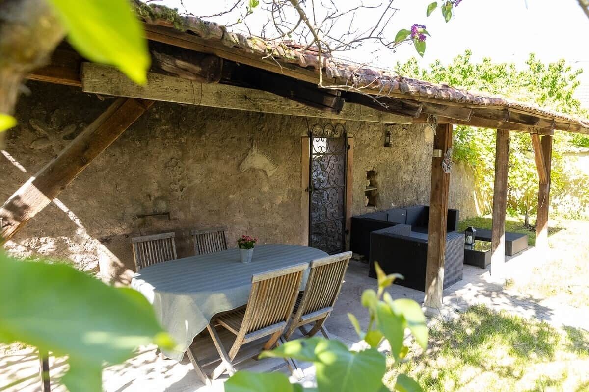 An outdoor patio area with a table and chairs, a wooden pergola, and a stone wall.