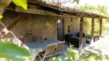 An outdoor patio area with a table and chairs, a wooden pergola, and a stone wall.