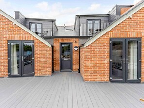 A modern building with a brick facade, two large sliding doors, and a balcony with a metal railing. - 2 Bed in Brockenhurst (oc-78729) (Brockenhurst)
