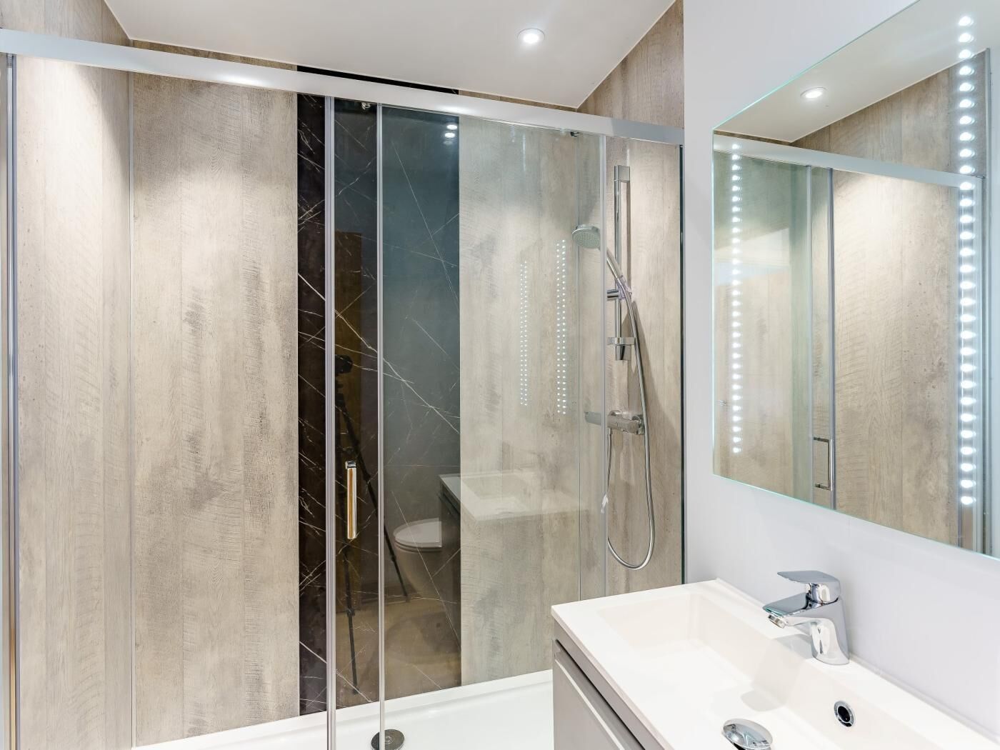 A modern bathroom with a glass-enclosed shower, a vanity with a mirror, and a recessed ceiling light.