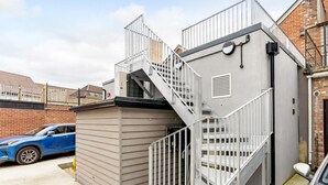 Een gebouw met een grijze gevel, een metalen trap en een klein afgesloten gedeelte met een deur.