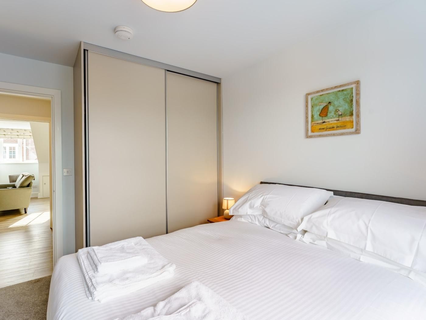 Ein Hotelzimmer mit einem Bett, einem Kleiderschrank, einem Gemälde und Blick auf ein weiteres Zimmer.