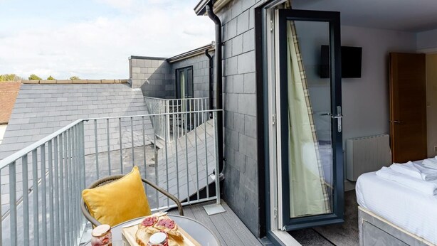 Een balkon met een tafel, een stoel en een bed in de aangrenzende kamer.