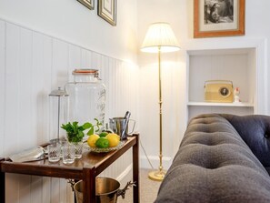 Ein Wohnzimmer mit einer Couch, einem Tisch mit Lampe, einem Radio und einem Regal mit einem gerahmten Bild.
