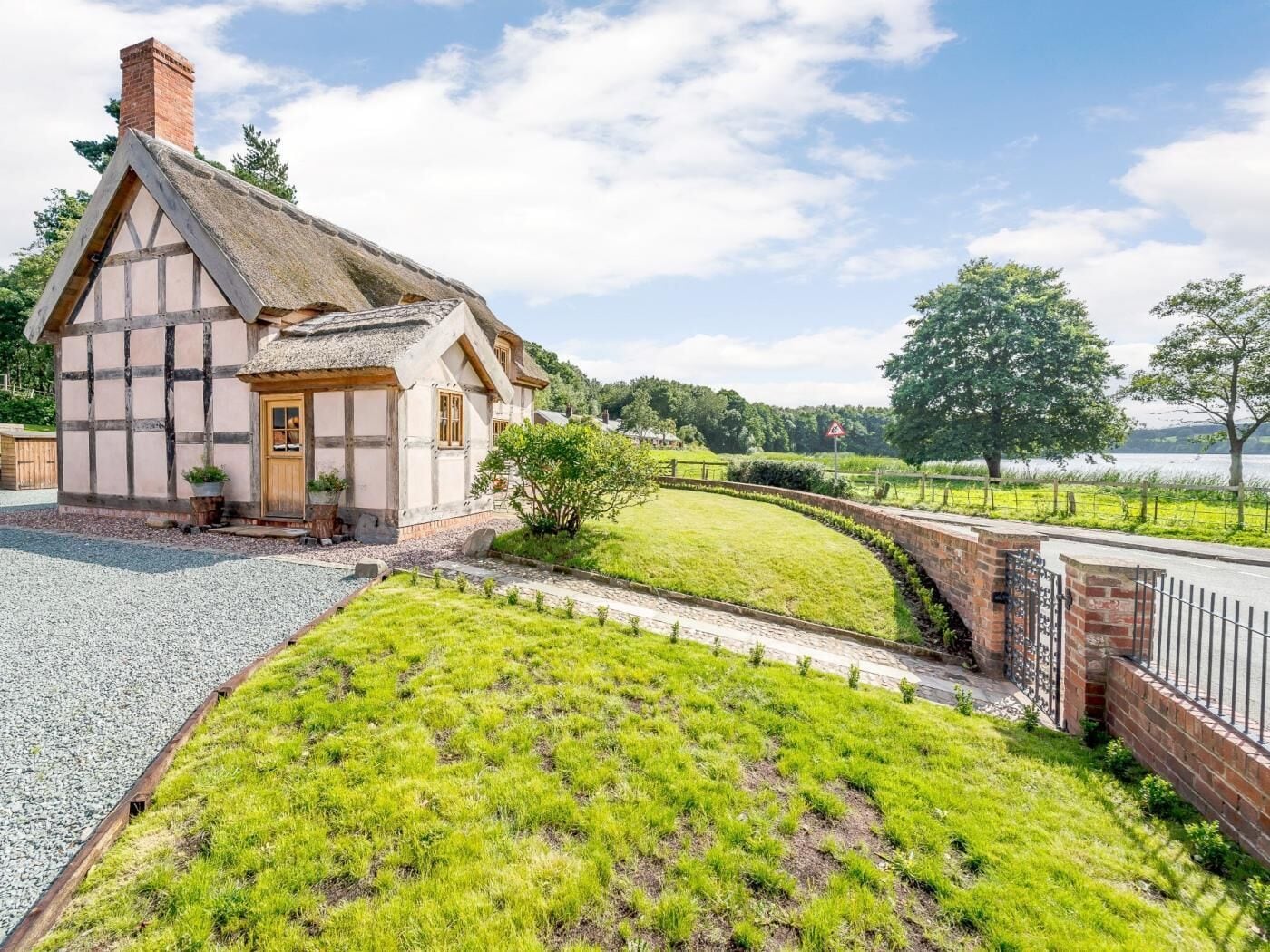A traditional half-timbered house with a thatched roof, a gravel driveway, and a grassy lawn.