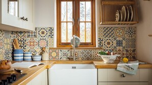Cocina con ventana, salpicadero de azulejos, encimera de madera, lavamanos blanco y armarios.
