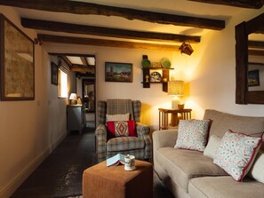 Un salon chaleureux avec un canapé, un fauteuil et un pouf, agrémenté d’une cheminée, d’œuvres d’art murales et d’une lampe.