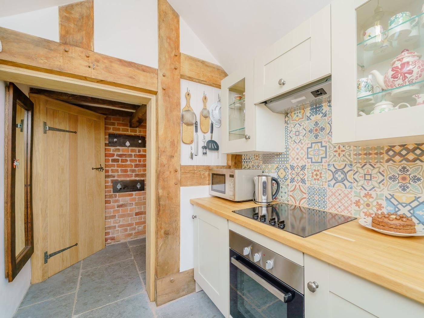Une cuisine avec un mur en briques, des poutres en bois, un four à micro-ondes, un four traditionnel et un dosseret carrelé.