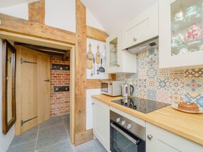 Une cuisine avec un mur en briques, des poutres en bois, un four à micro-ondes, un four traditionnel et un dosseret carrelé.