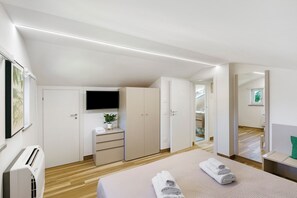 A modern bedroom with a bed, a TV, a wardrobe, and a desk with a plant.