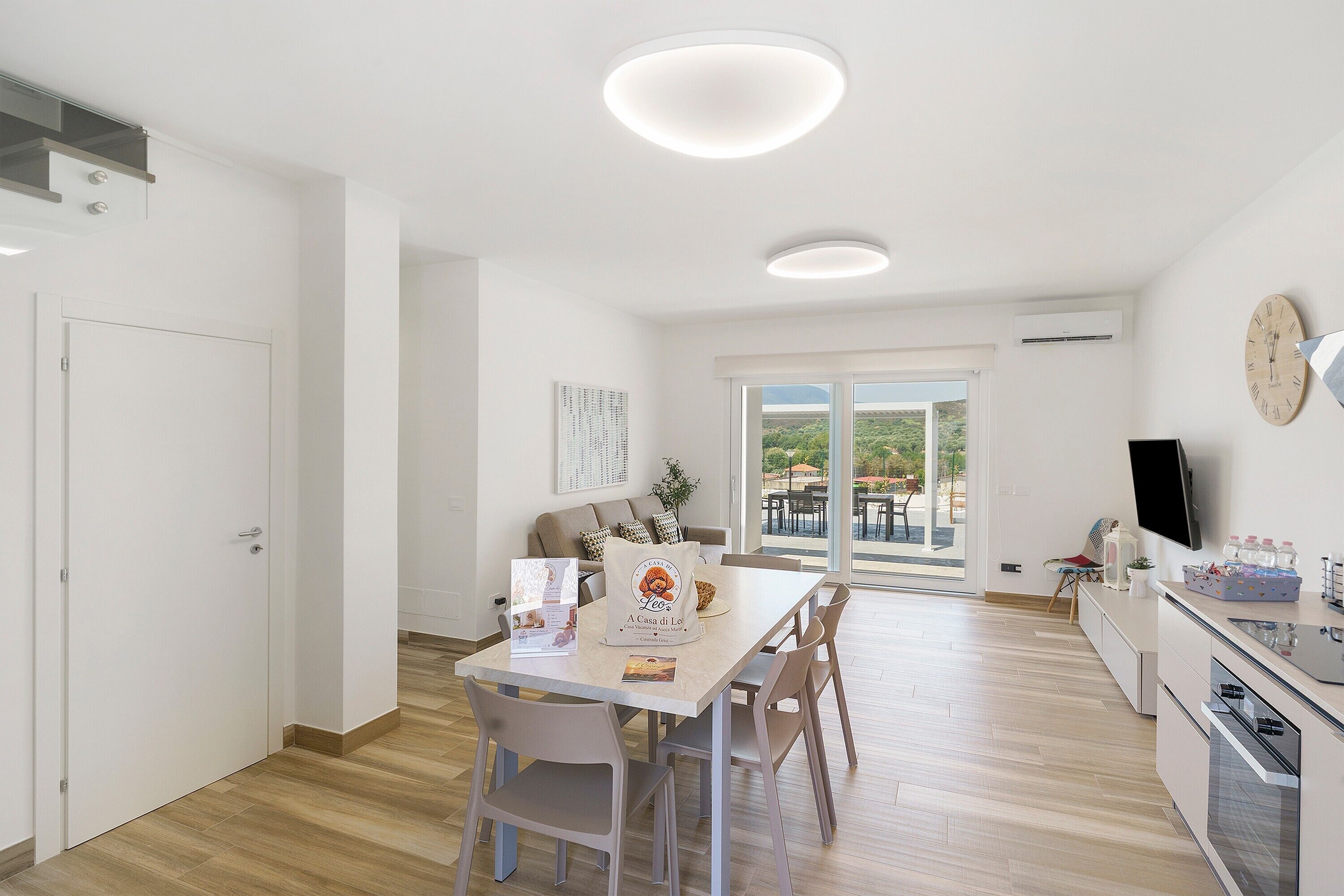 A modern kitchen with a dining area, a large window, and a flat-screen TV.