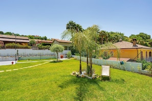 Zona residencial amb un jardí ben cuidat, un arbre petit i un edifici amb teulada enrajolada.
