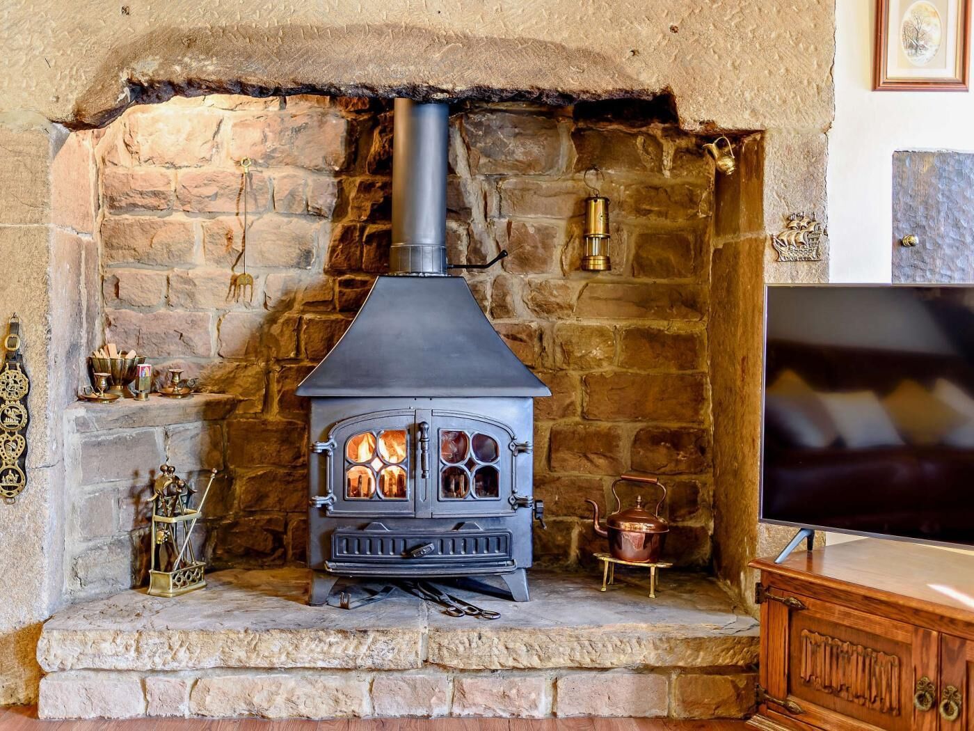 Una chimenea de piedra con estufa de leña, un televisor sobre un mueble bajo y adornos en la repisa.
