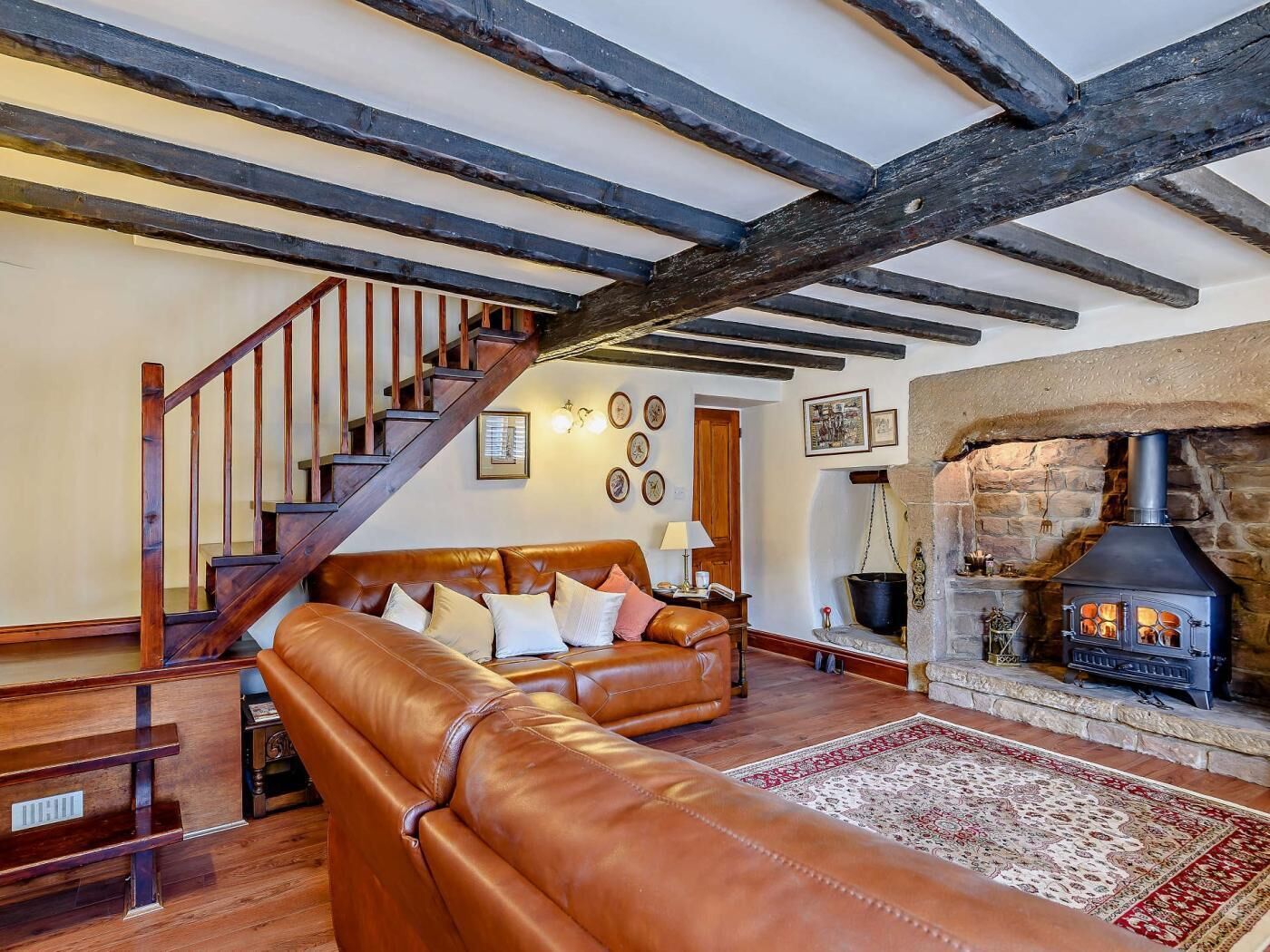 A cozy living room with a leather sofa, a stone fireplace, and exposed wooden beams.