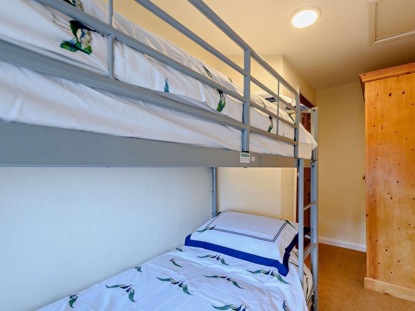 Una cama litera con ropa blanca y un cabecero azul, un armario de madera y una lámpara en el techo.