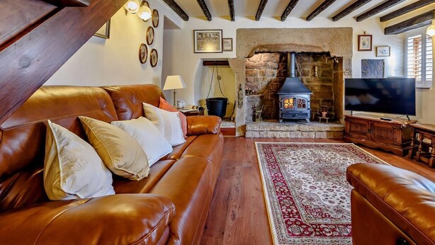 A cozy living room with a leather sofa, a stone fireplace, and a television. - 2 Bed in Matlock (oc-81116) (Crich)