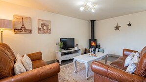 Ein Wohnzimmer mit Ledersofas, einem weißen Couchtisch, einem Fernseher, einem Kamin und Wandbildern mit Eiffelturm-Motiv.