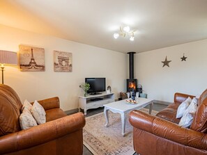 Ein Wohnzimmer mit Ledersofas, einem weißen Couchtisch, einem Fernseher, einem Kamin und Wandbildern mit Eiffelturm-Motiv.
