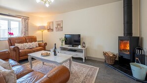 Ein Wohnzimmer mit einer Couch, einem Couchtisch, einem Fernseher, einem Kamin und einem Fenster mit Vorhängen.
