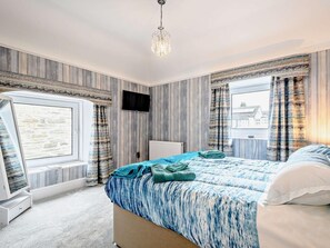 A bedroom with a bed, a TV, a window, and a chandelier.