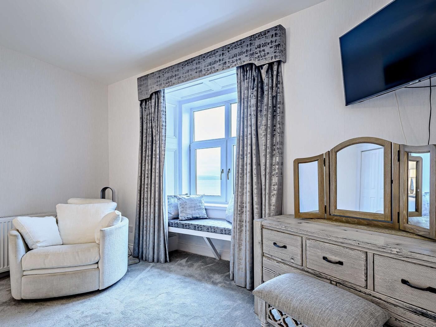 Een slaapkamer met een bed, een kaptafel met spiegel, een stoel en een raam met gordijnen.