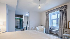 Habitación de hotel moderna con una cama grande, zona de estar junto a la ventana y un baño con ducha.