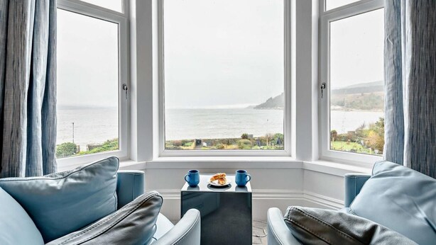 Una habitación con dos sofás de cuero azul orientados hacia una ventana grande con vista al mar y una colina distante.