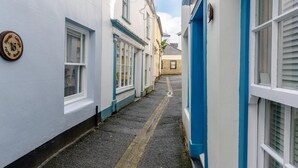 Een smalle straat met witte en blauwe gebouwen, een zichtbaar huisnummer, en een heldere lucht.