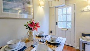 Een eetruimte met een tafel voor vier personen, een vaas met bloemen en een deur met raam.