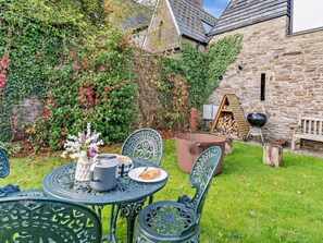 A patio with a table set for two, surrounded by greenery and stone walls.
