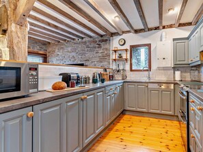 A kitchen with a stone wall, wooden beams, a Bosch microwave, and a wooden floor.
