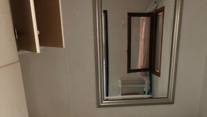 Pieni huone, jossa on yksi sänky, pelkistetty patja, peili ja pieni kaappi.