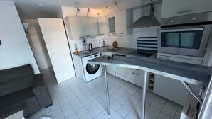 Moderni keittiö, jossa on valkoiset kaapit, ruostumattomasta teräksestä valmistetut kodinkoneet ja harmaa työtaso.