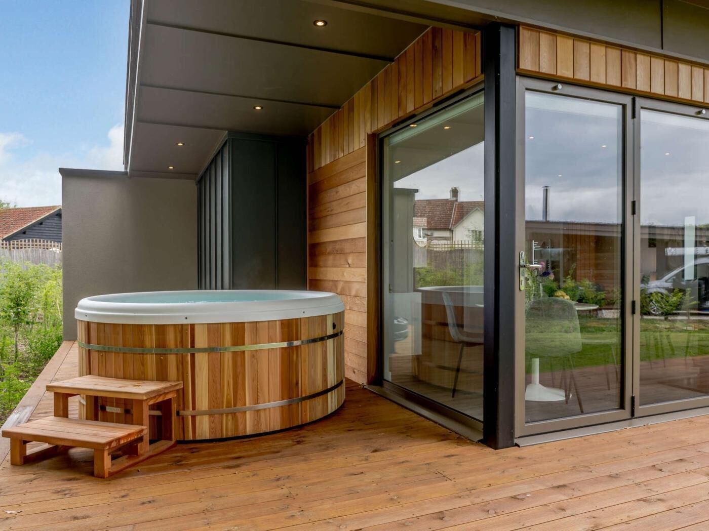 A wooden deck with a hot tub, a glass door, and a wooden bench.