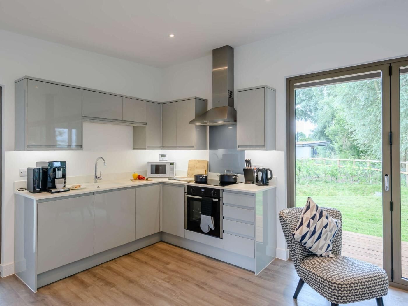 A modern kitchen with grey cabinets, a built-in oven, a microwave, and a coffee maker.